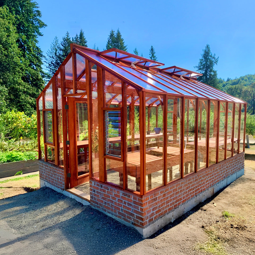 Glass greenhouse with brick foundation in a garden setting