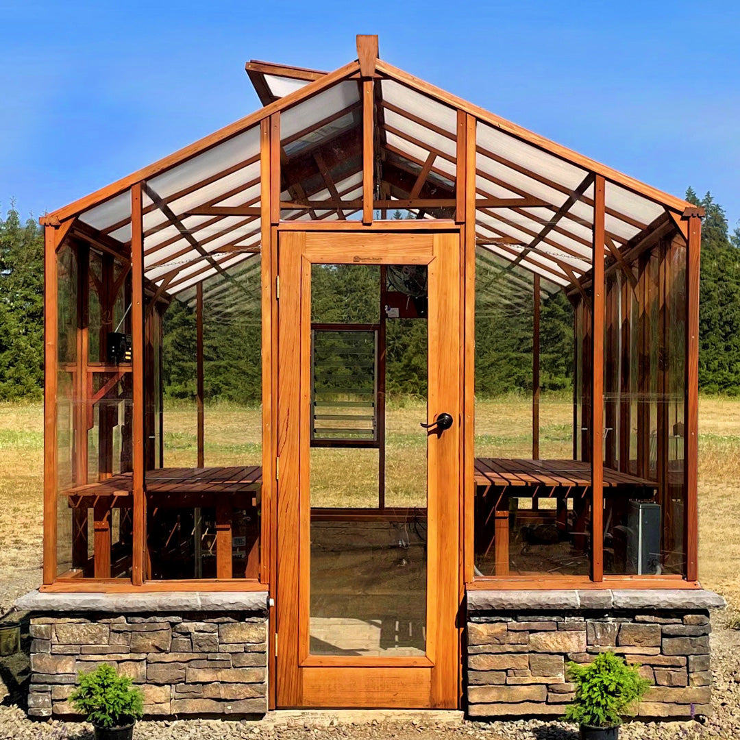 Wooden greenhouse with stone foundation in a field with trees in the background