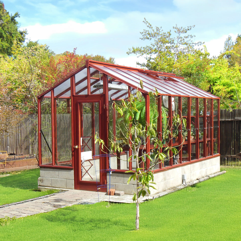 Glass greenhouse with red frame in a garden setting