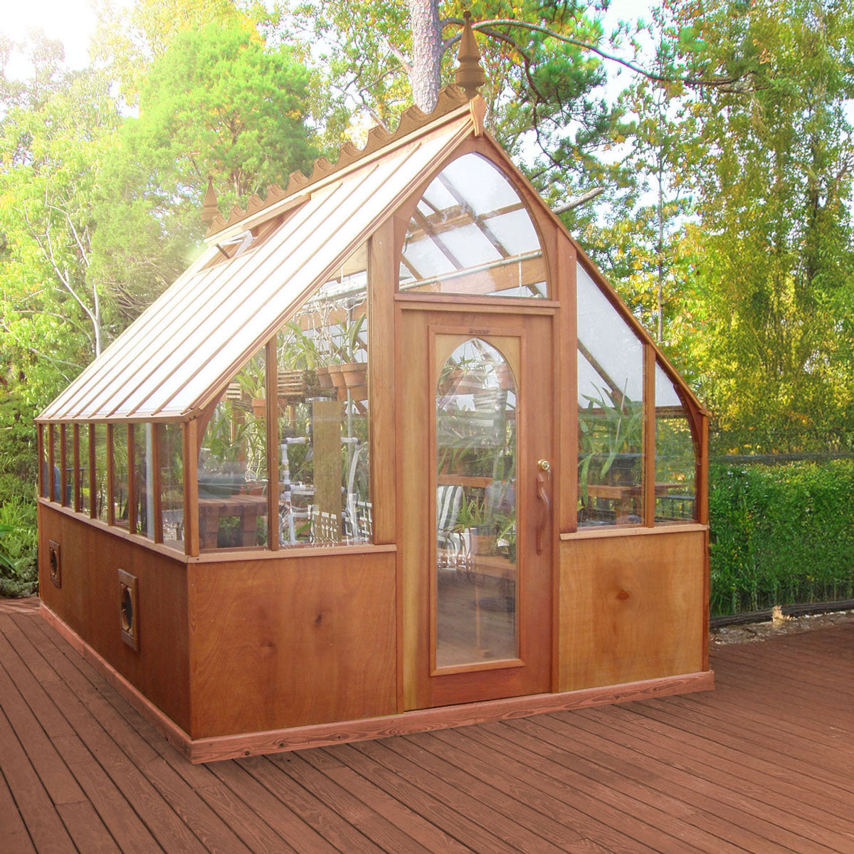 Wooden greenhouse with glass panels on a wooden deck surrounded by trees