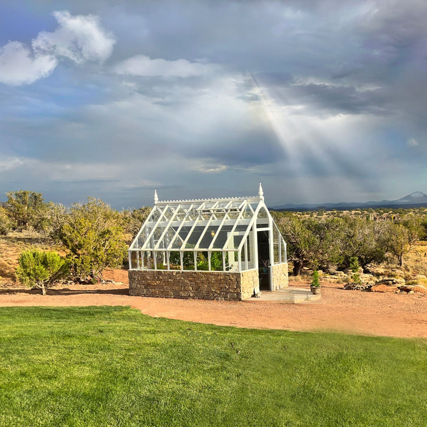 Glass greenhouse in a desert landscape with a rainbow in the background