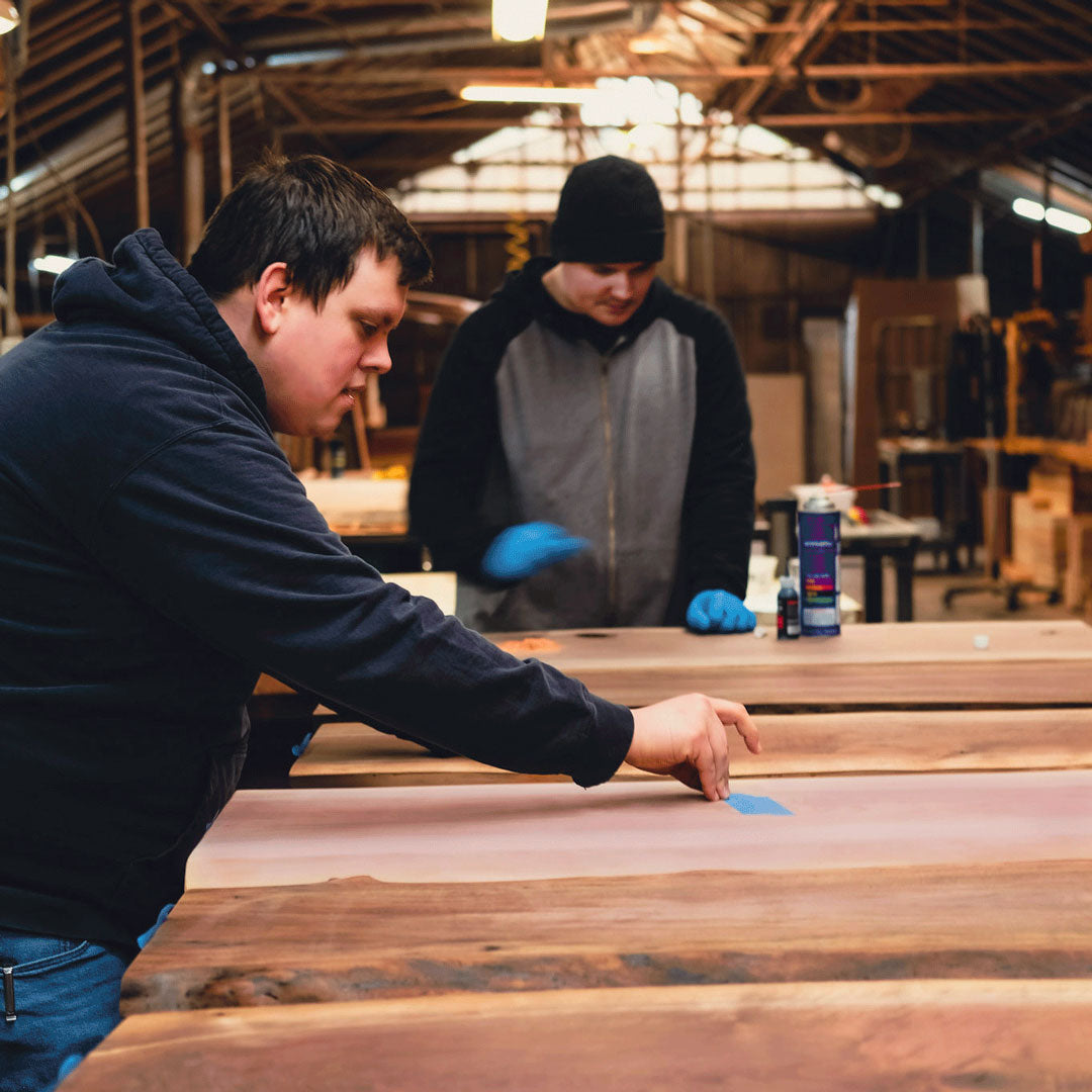 Two people working on wooden slab tables in a workshop setting.