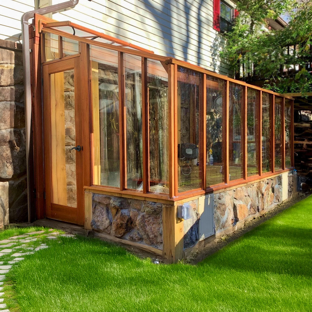 Wooden greenhouse attached to a house with stone foundation