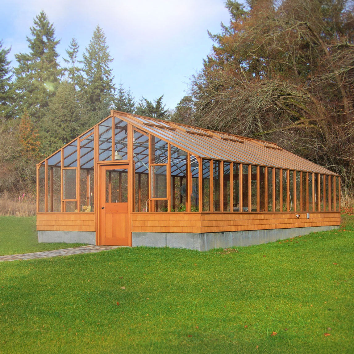 Wooden greenhouse with glass panels in a grassy area with trees