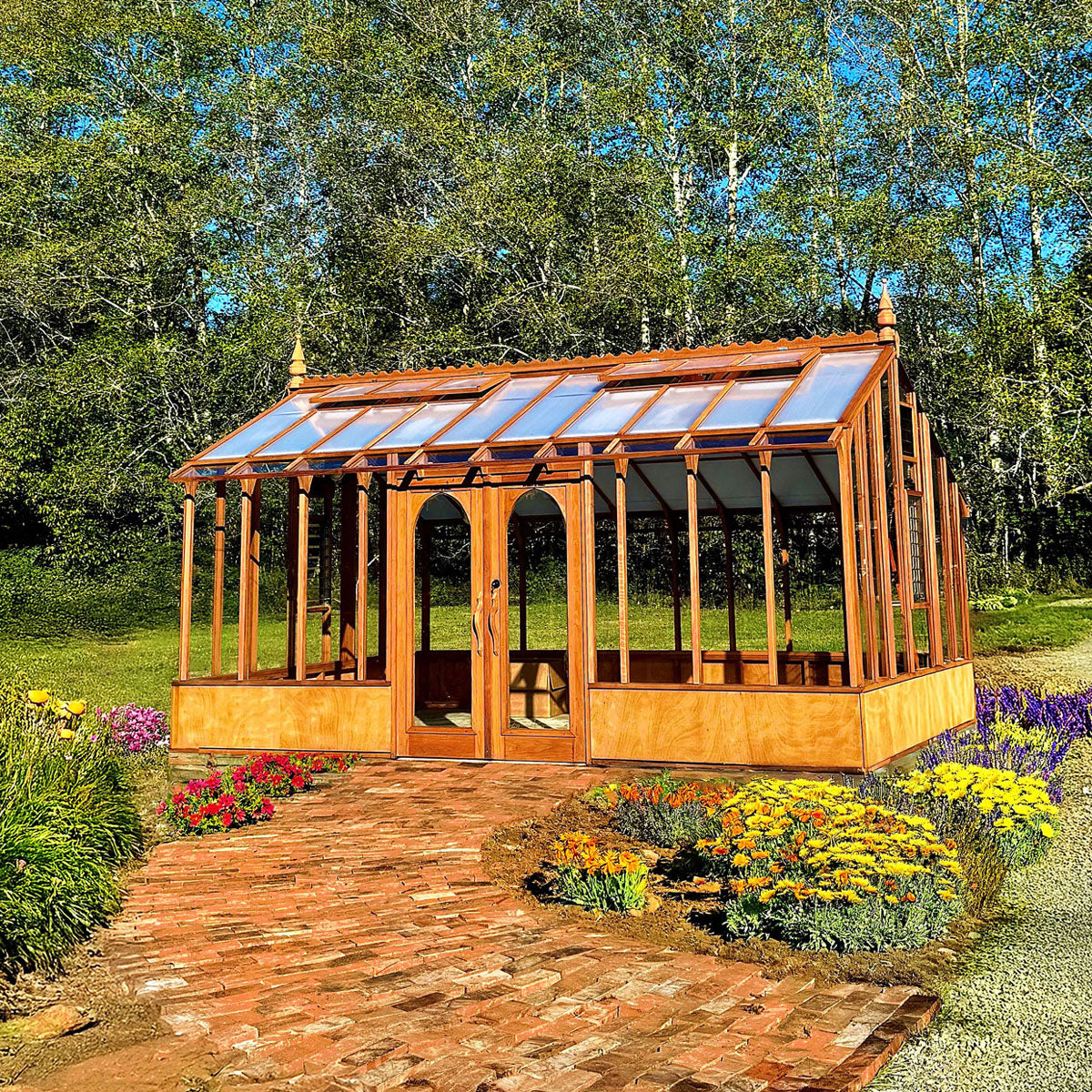 Wooden greenhouse with glass panels in a garden setting with flowers and trees.